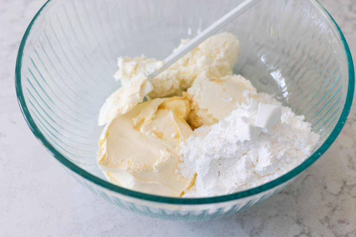 The mascarpone cheese, ricotta, and powdered sugar are in a mixing bowl with a spoon.
