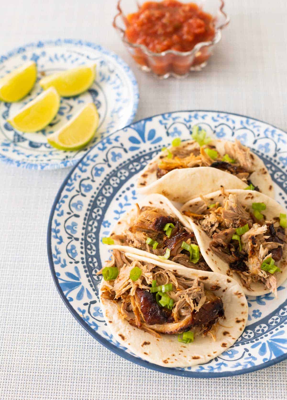 The plate of tacos sits next to a plate of lime wedges and a bowl of salsa.