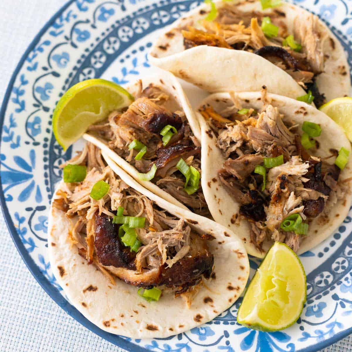 The plate of pork carnitas tacos have fresh lime wedges and green onions sprinkled over the top.