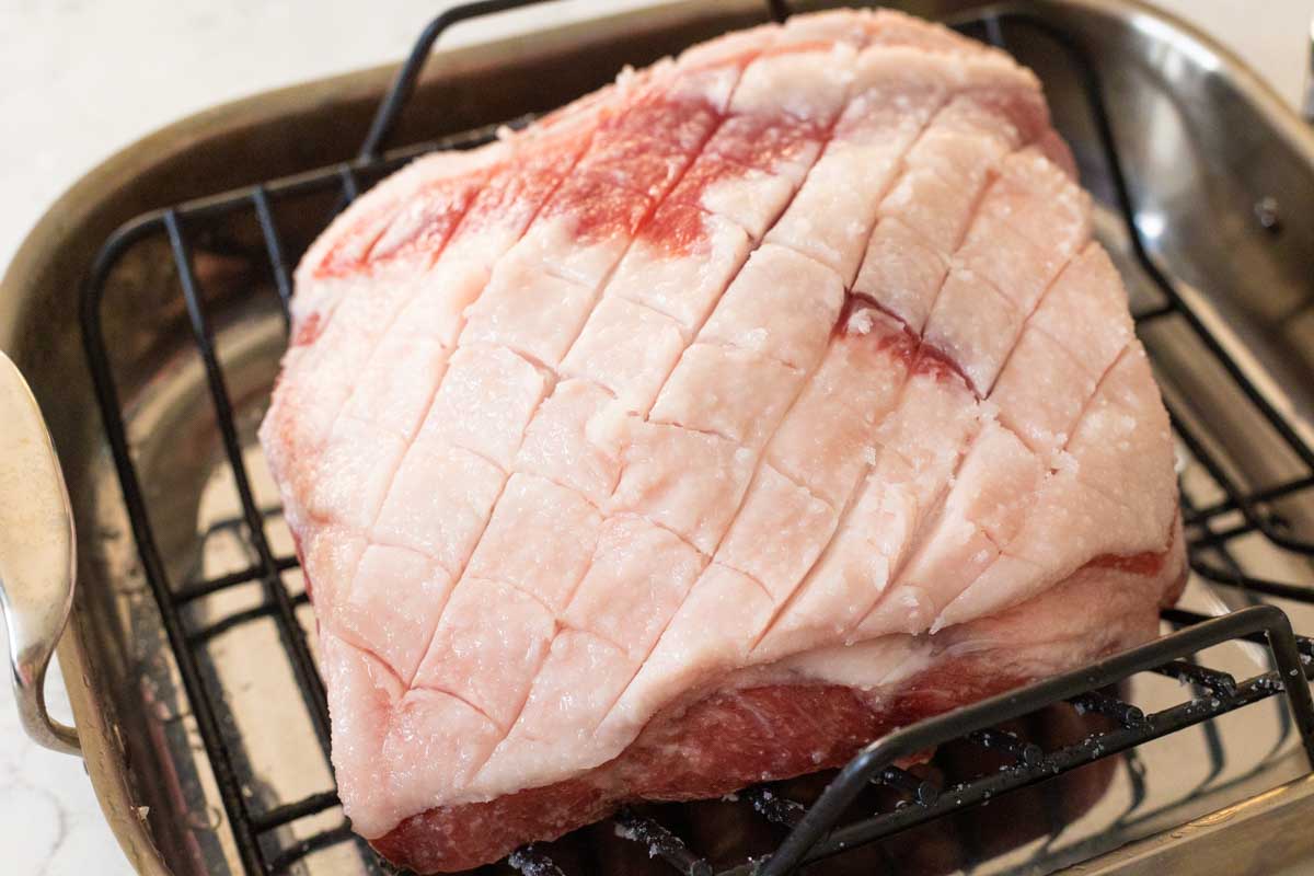 The top layer of the pork roast has been scored with a paring knife to make cross hatch marks.
