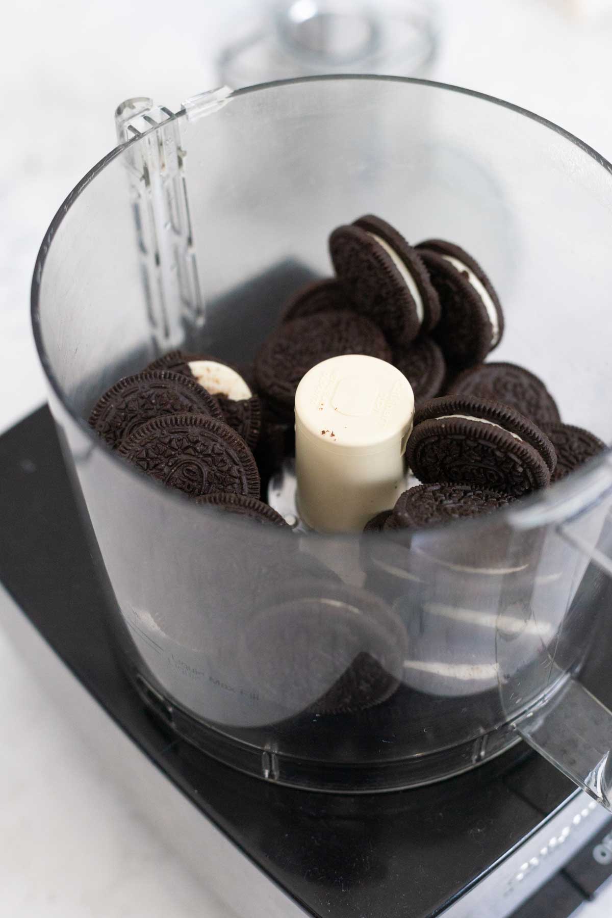 The Oreo cookies have been added to the bowl of a food processor.