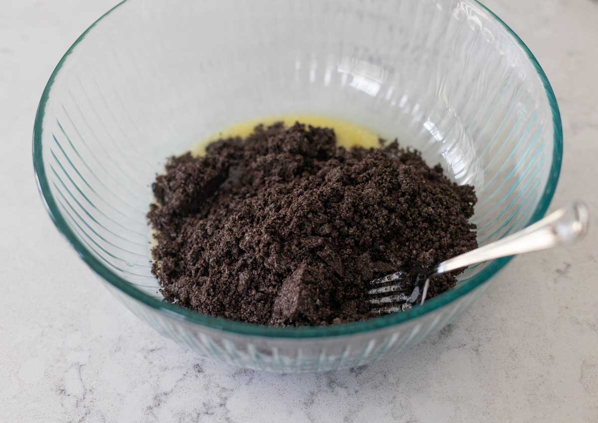 The mixing bowl shows the Oreo cookie crumbs being mixed together with melted butter.
