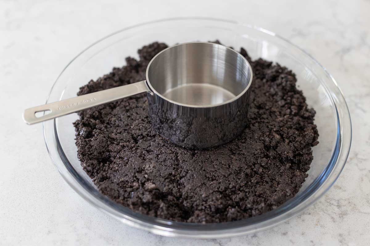 The Oreo cookie crumbs are being patted into place with a measuring cup.