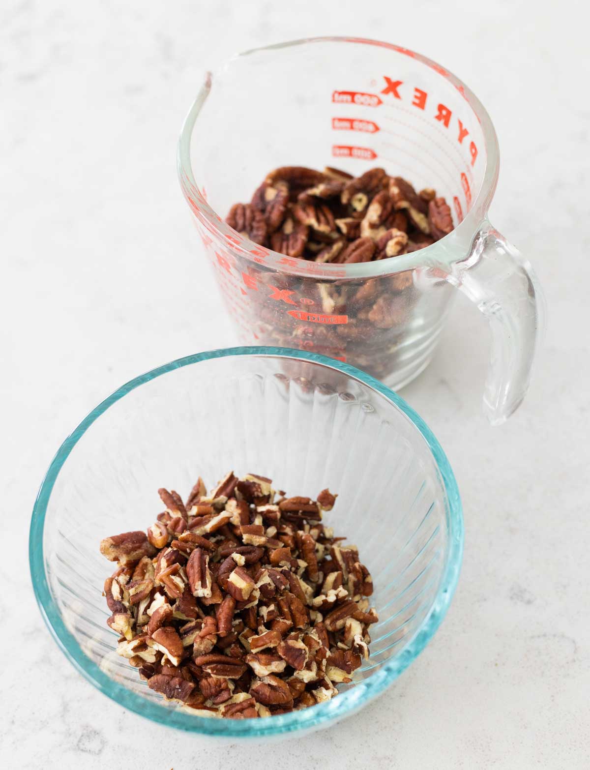 A mixing bowl has chopped pecans and a measuring cup has whole pecan halves.