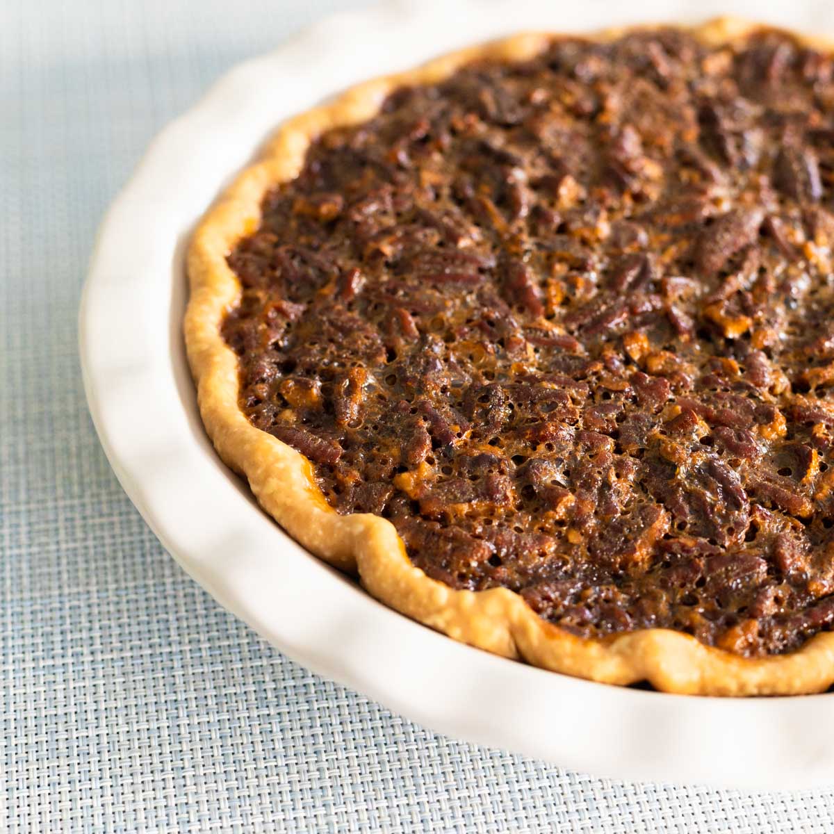 The homemade pecan pie is in a white pie dish on a blue background.