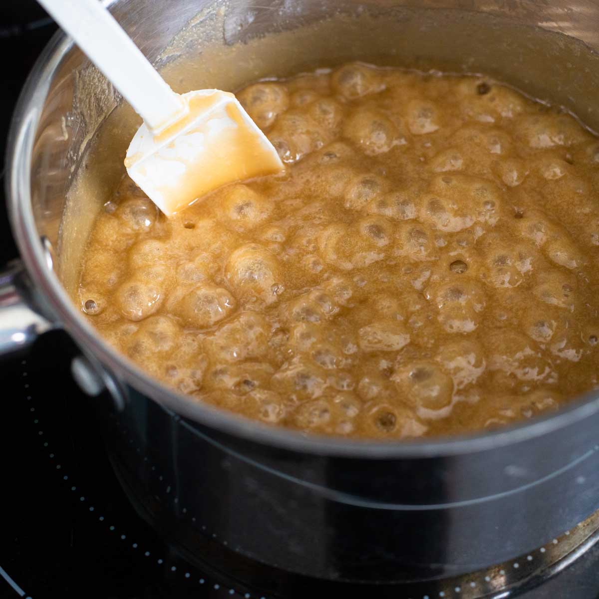 The brown sugar and Karo syrup are bubbling and a white spatula is stirring the mixture.