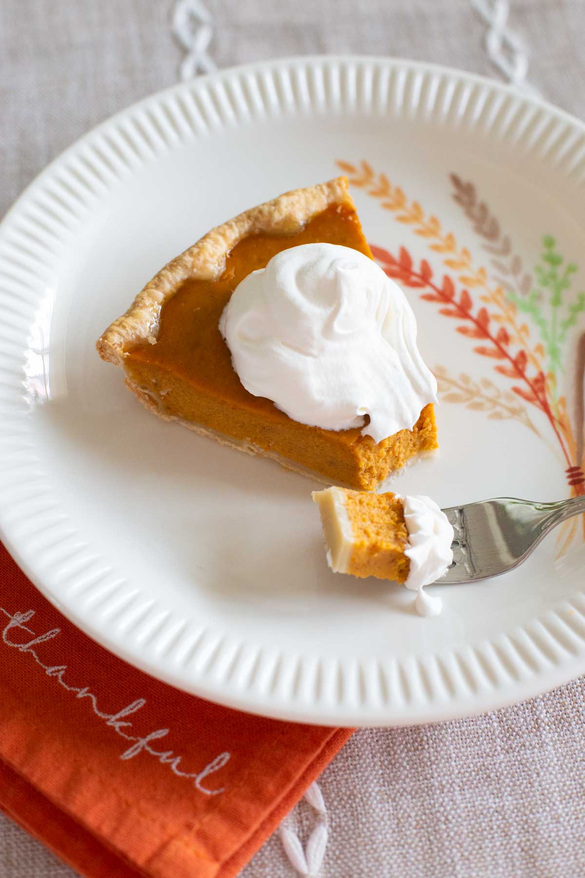 The slice of pumpkin pie is on a fall plate with an orange napkin that says "Thankful."