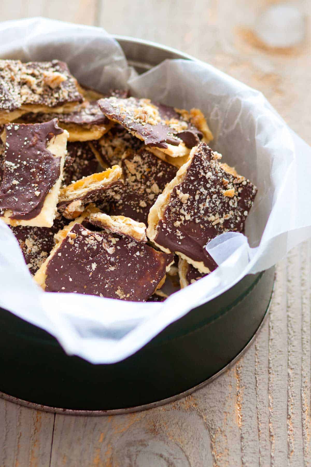 The toffee is in a cookie tin with white parchment paper lining.