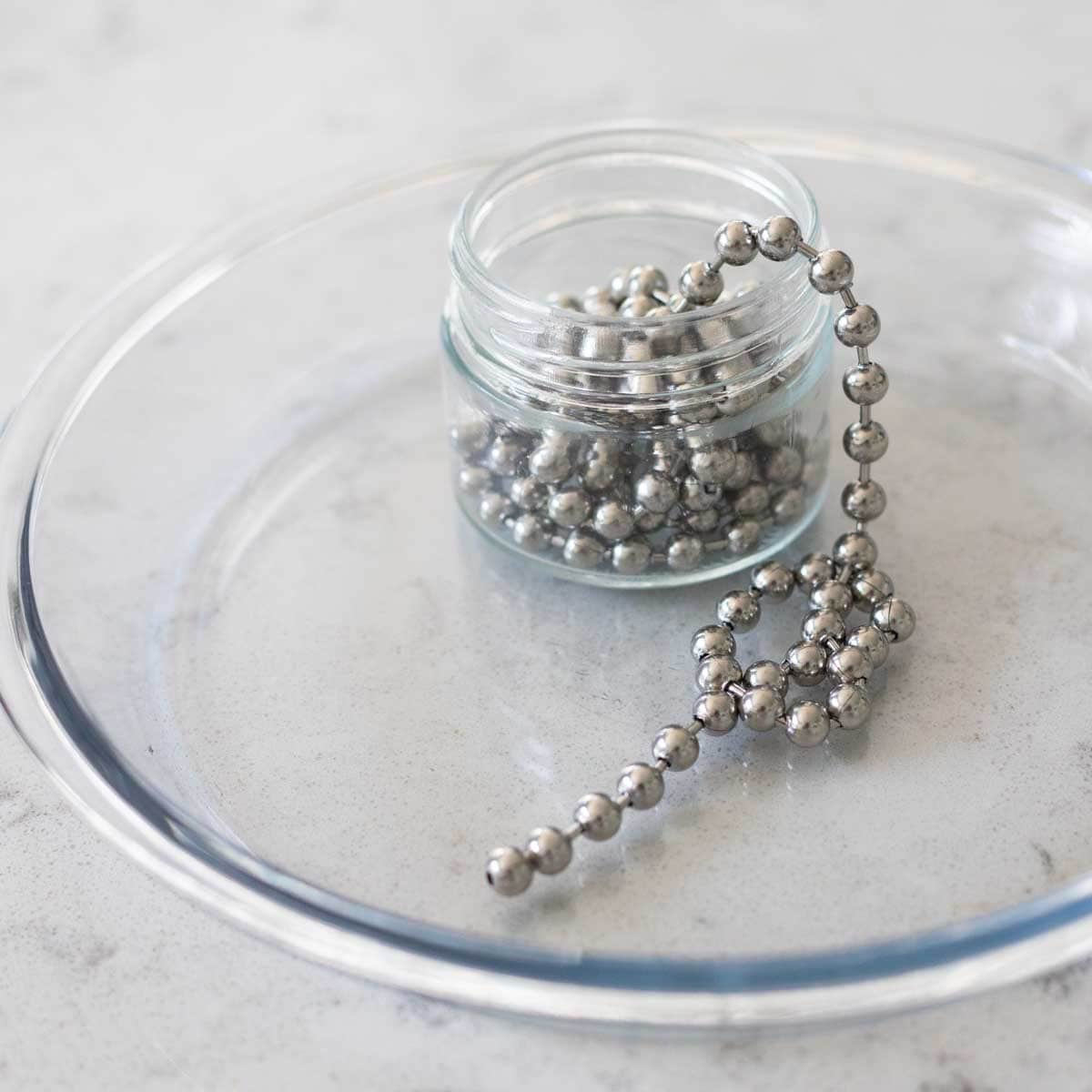 An empty pie dish has a container holding a metal pie chain.