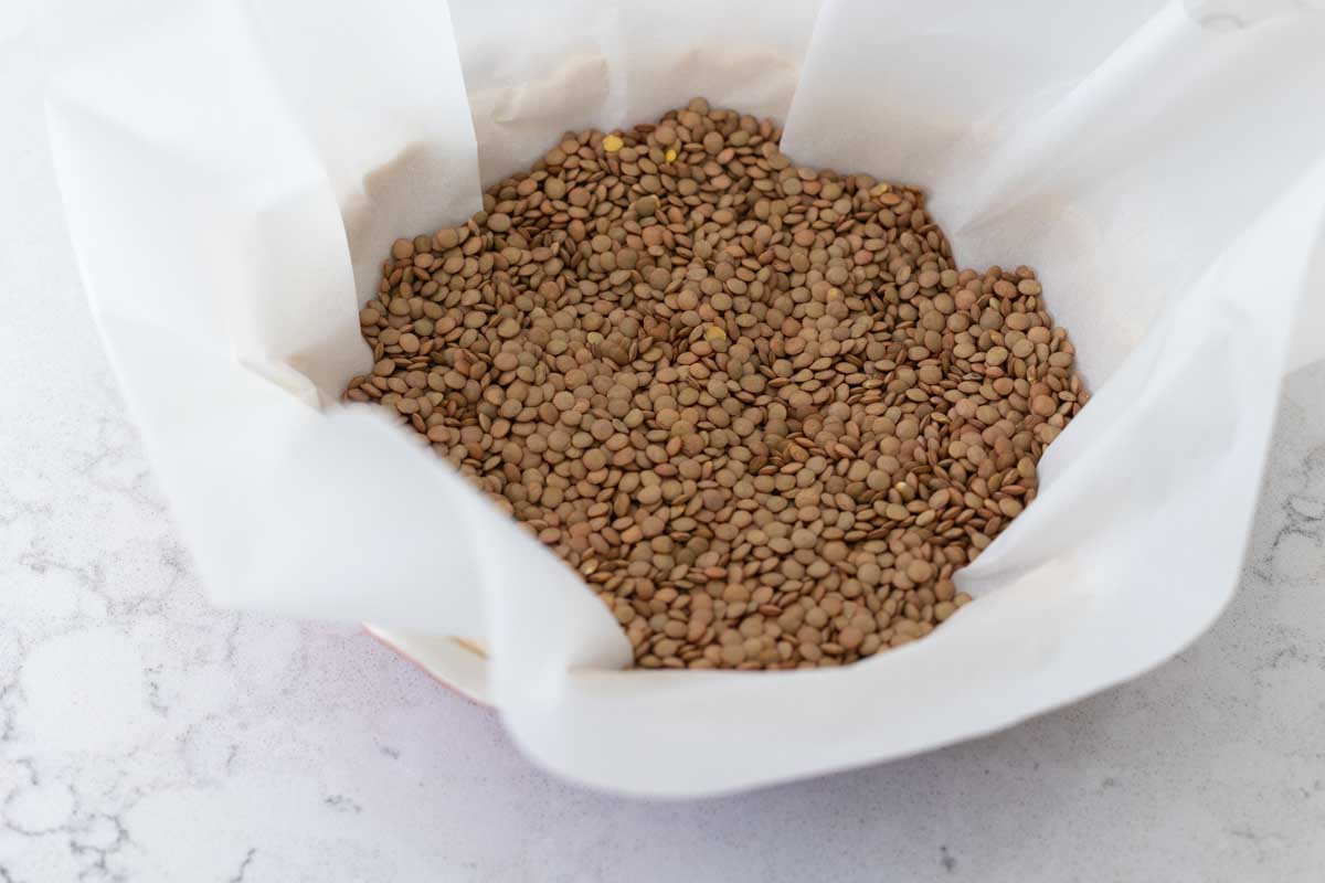 A pie crust is weighted down by lentils in parchment paper.