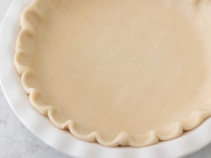 A white pie plate has a ruffled pie crust waiting to be filled with pie filling.