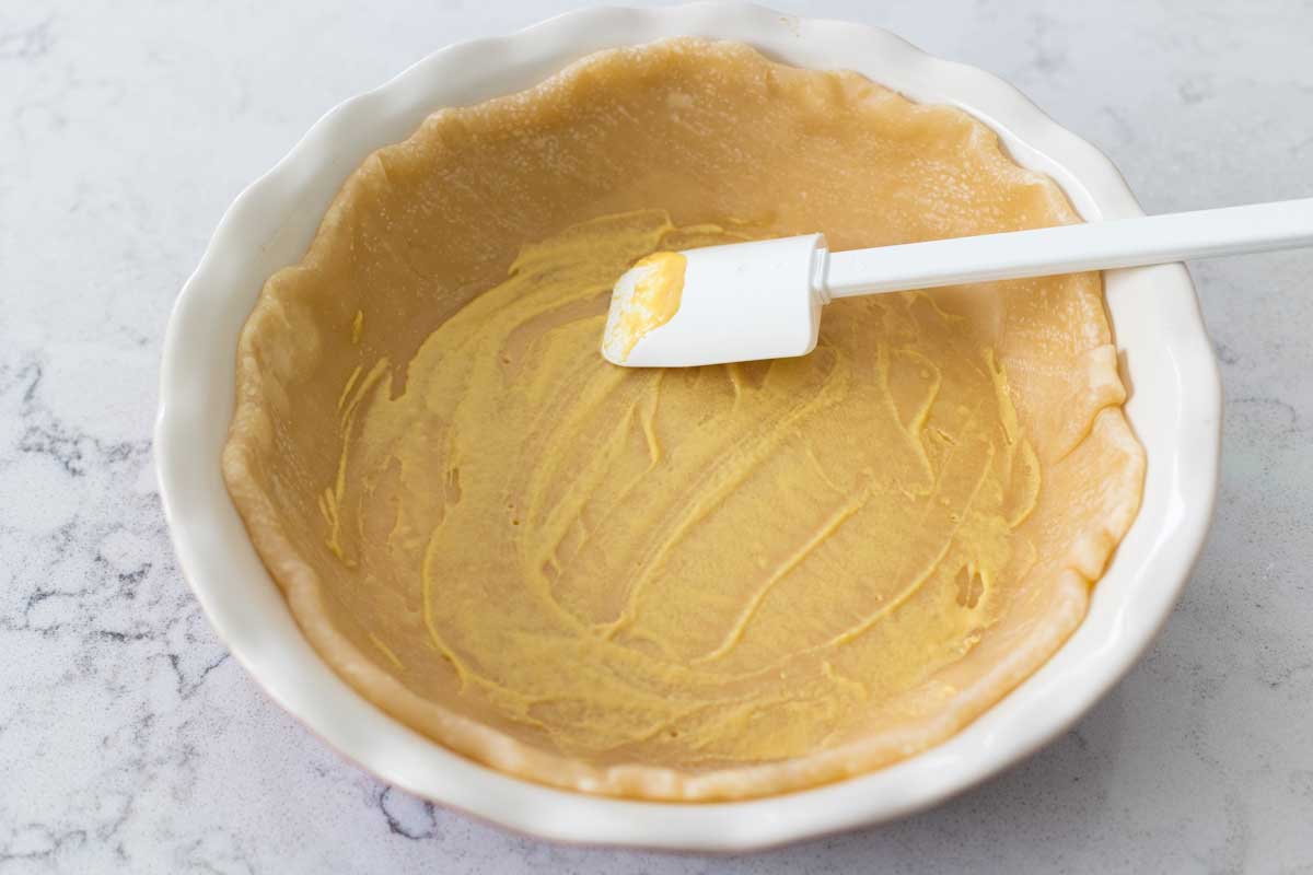 The pie crust has mustard smoothed all over it with a white spatula.