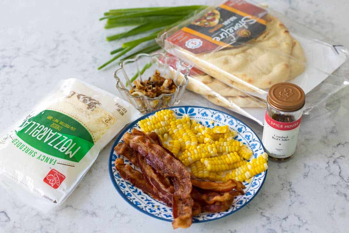 The ingredients to make a sweet corn pizza are on the counter.