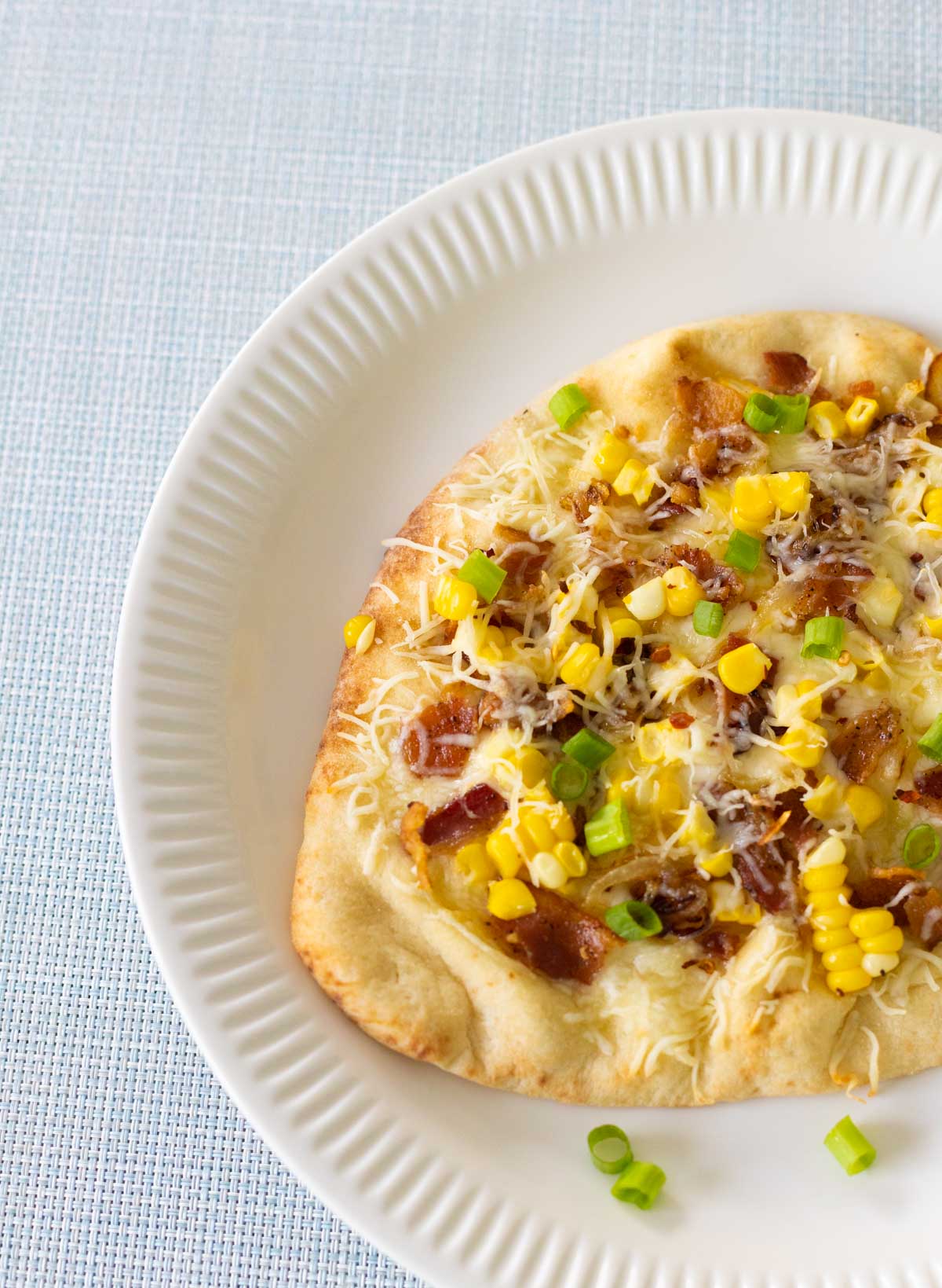 The baked sweet corn pizza is being served on a white plate.