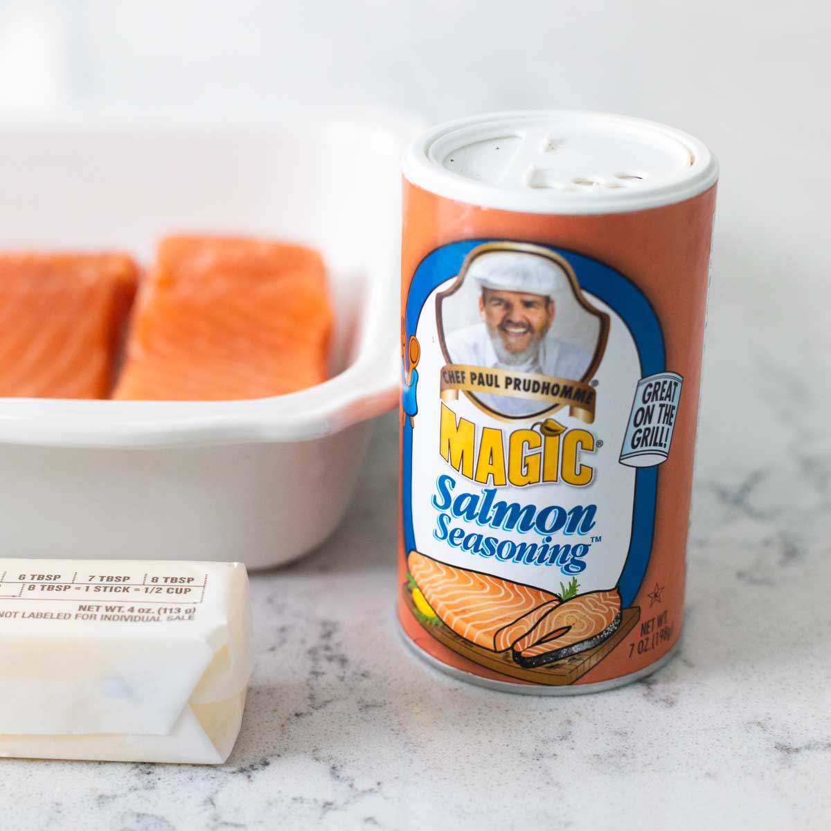 The bottle of salmon seasoning sits next to a baking pan of salmon.
