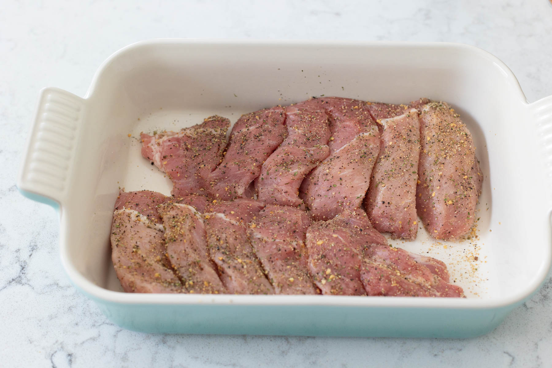 The pork has been coated in seasoning and placed in a baking dish.