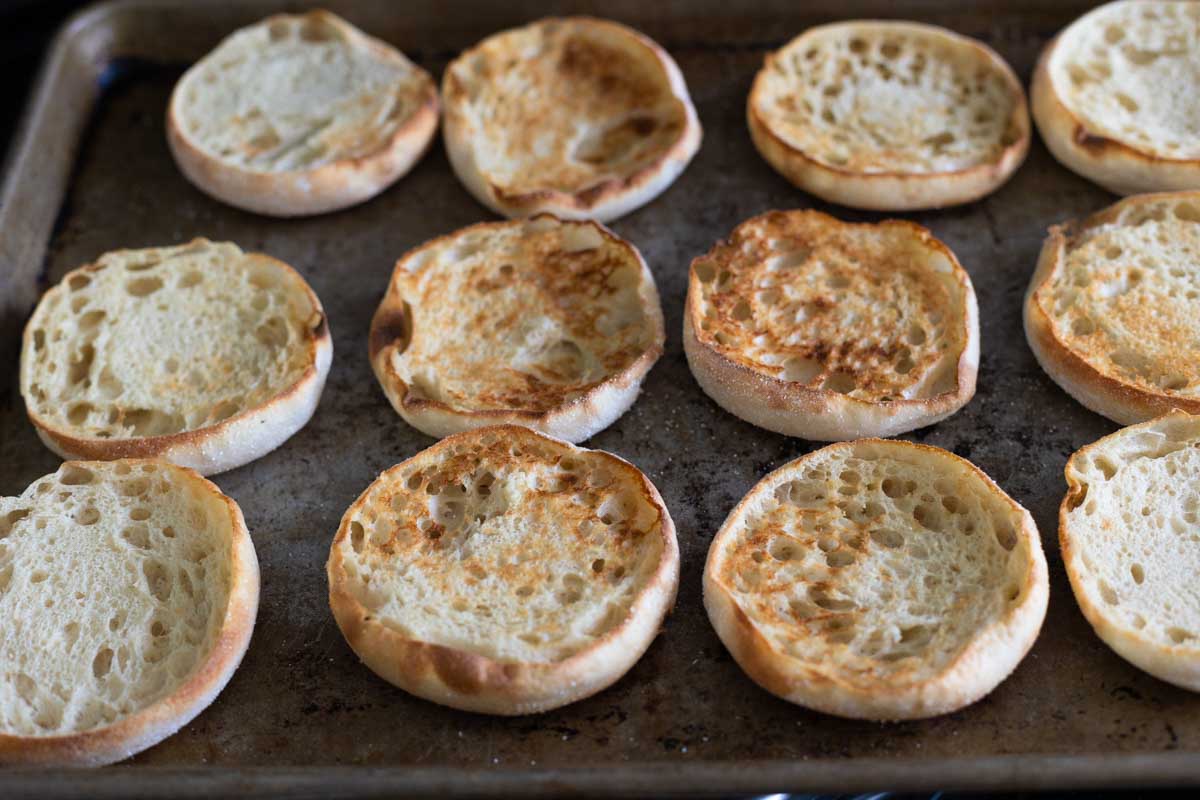 A baking pan is filled with open face English muffins fresh from the broiler. They have golden brown toasted tops.