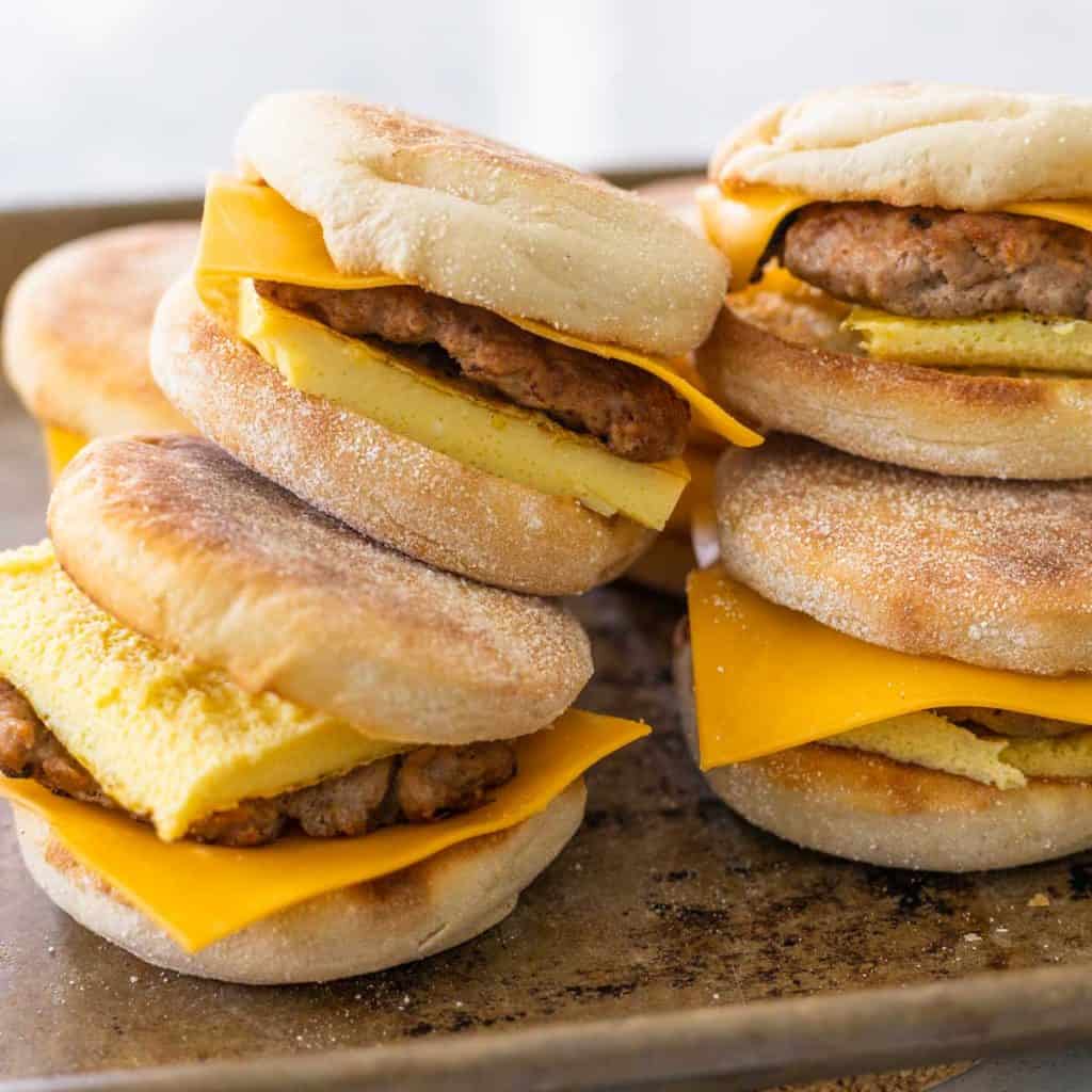 A pile of sausage and egg english muffin sandwiches are ready to be wrapped for the freezer.