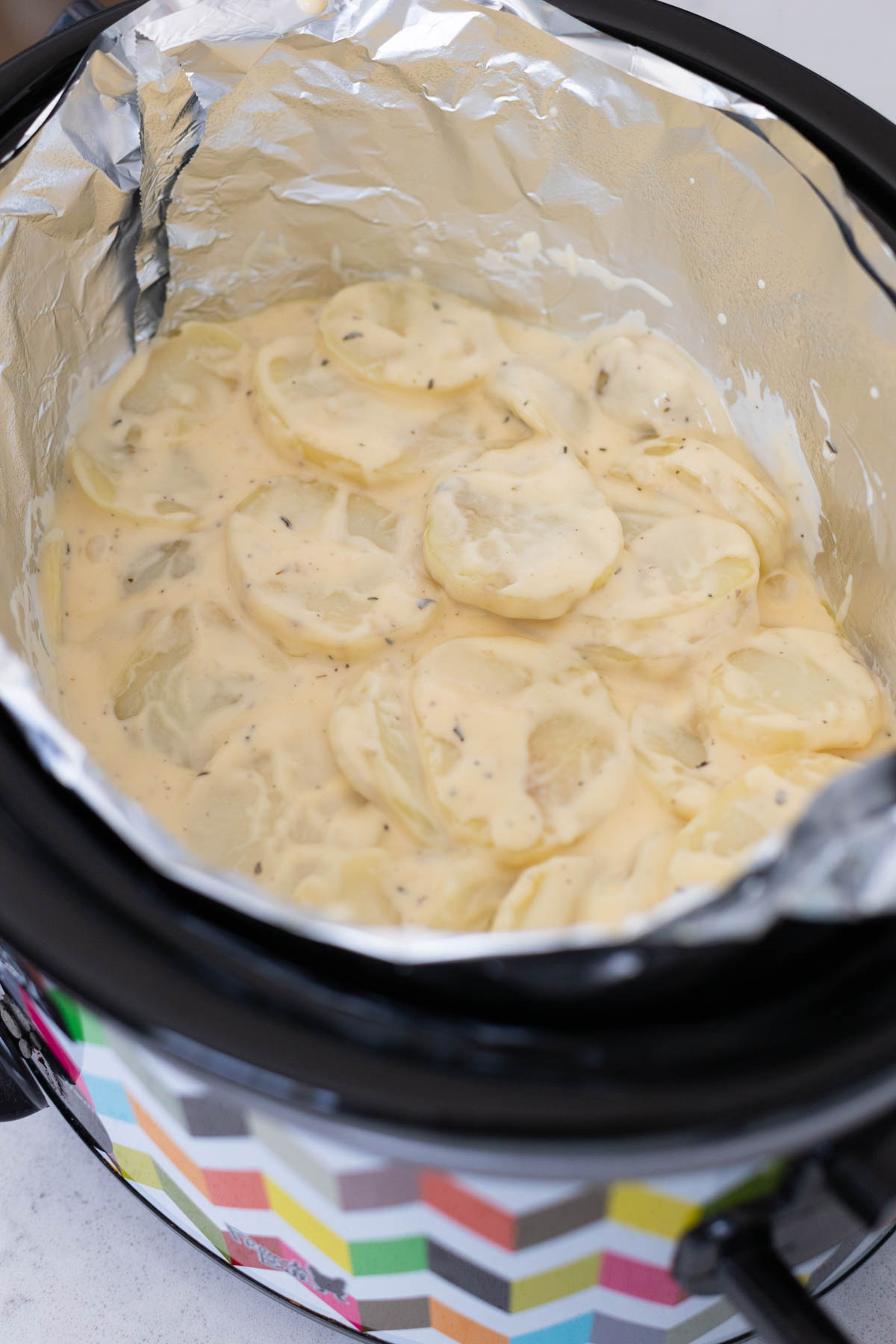 The prepared scalloped potatoes have been added to the slowcooker pot and spread into a compact layer.