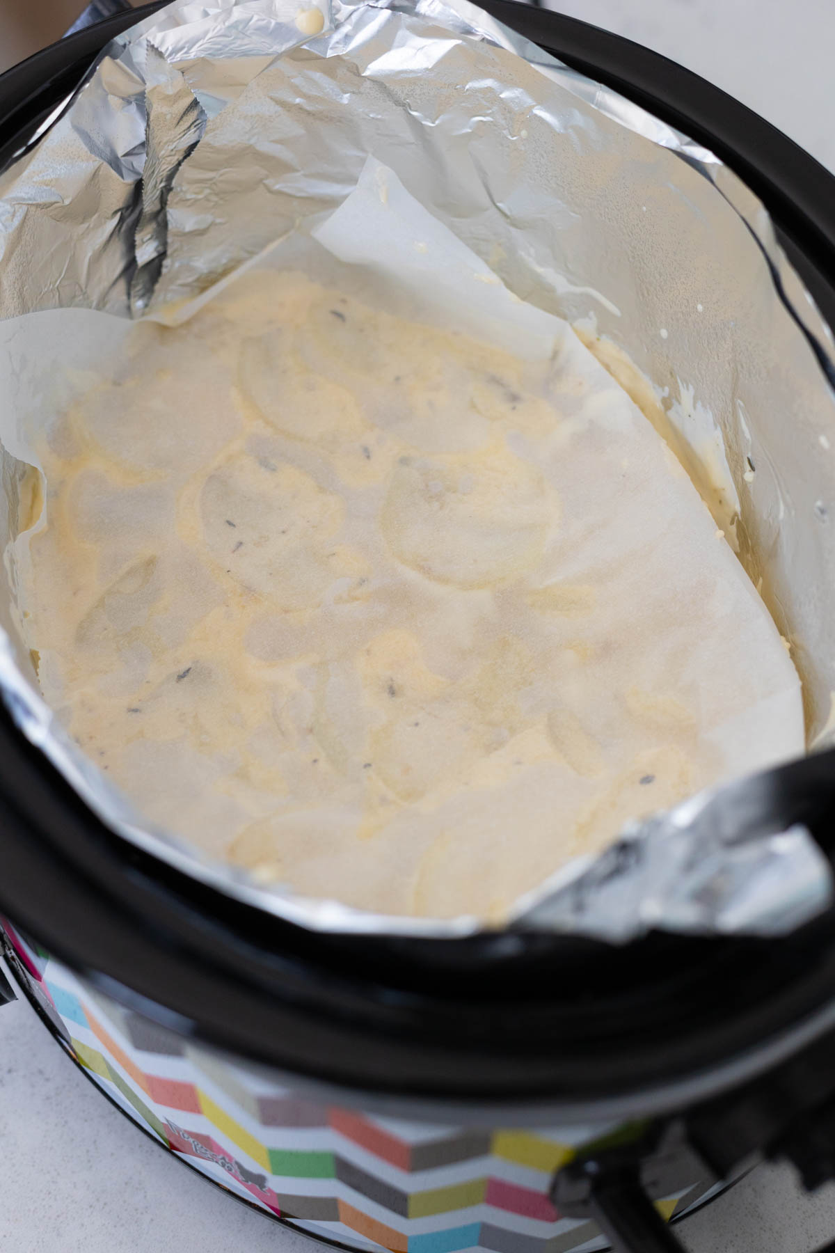 A piece of parchment that has butter rubbed on it has been smoothed over the top of the potatoes in the slowcooker.