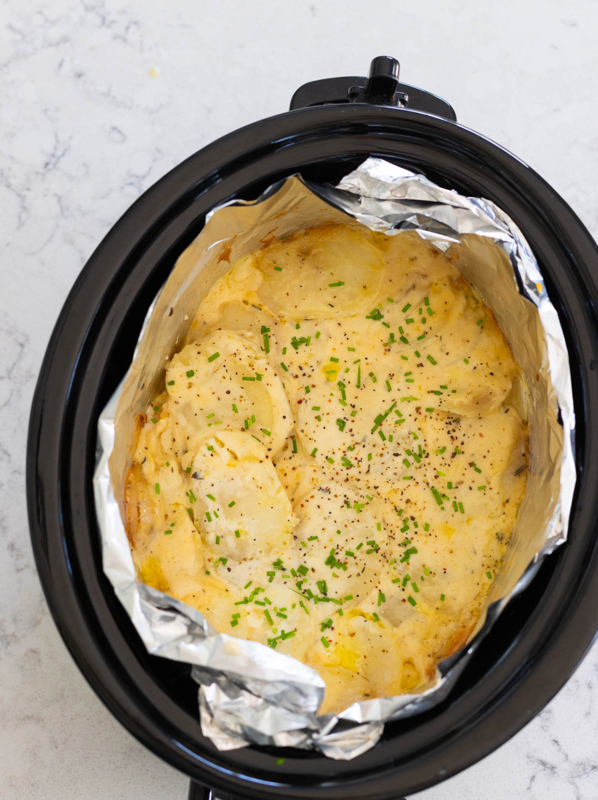 The finished scalloped potatoes have a golden yellow color with crispy edges and fresh chives sprinkled over the top.