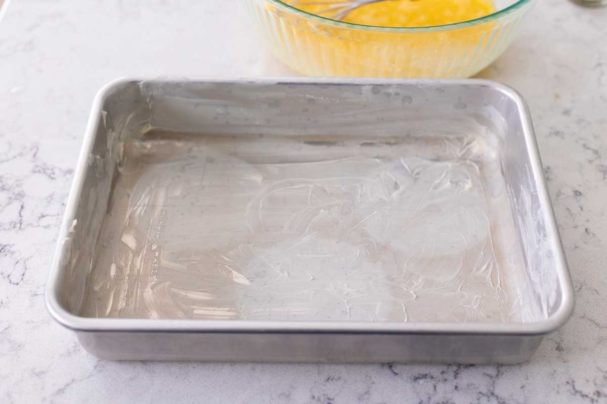 The metal 9 x 13-inch baking pan has a thick coat of butter spread over the bottom.