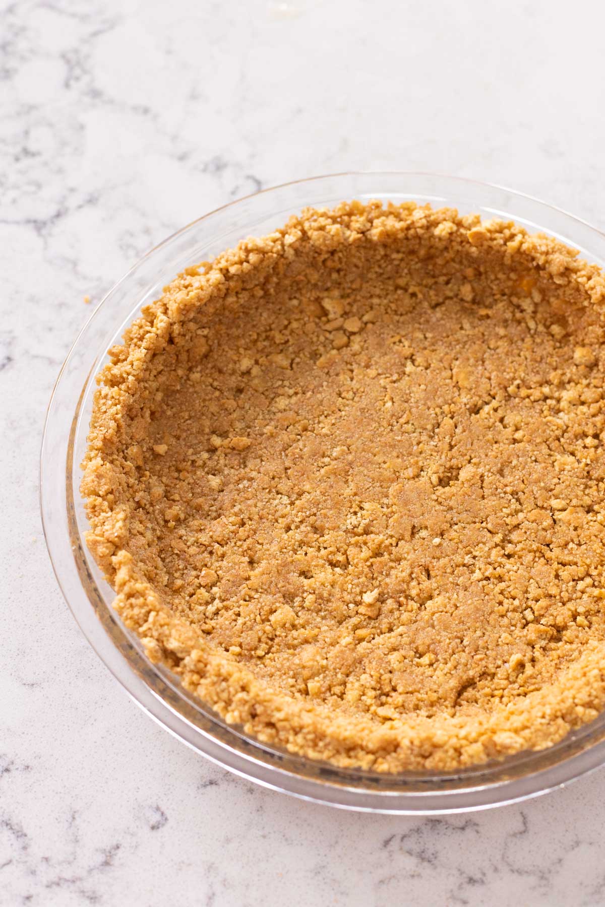 A pie plate has a golden brown graham cracker crust ready to be topped with pie filling.