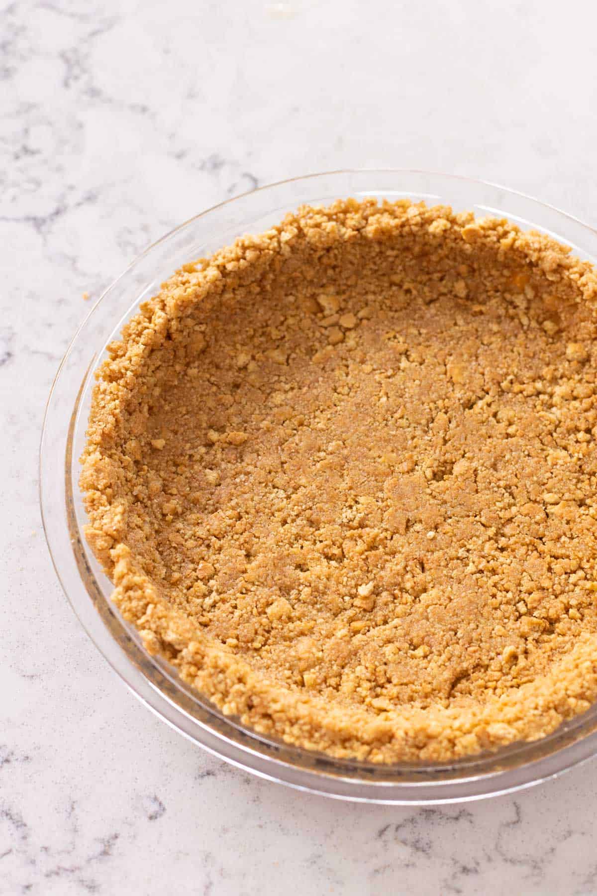 A pie plate has a golden brown graham cracker crust ready to be topped with pie filling.