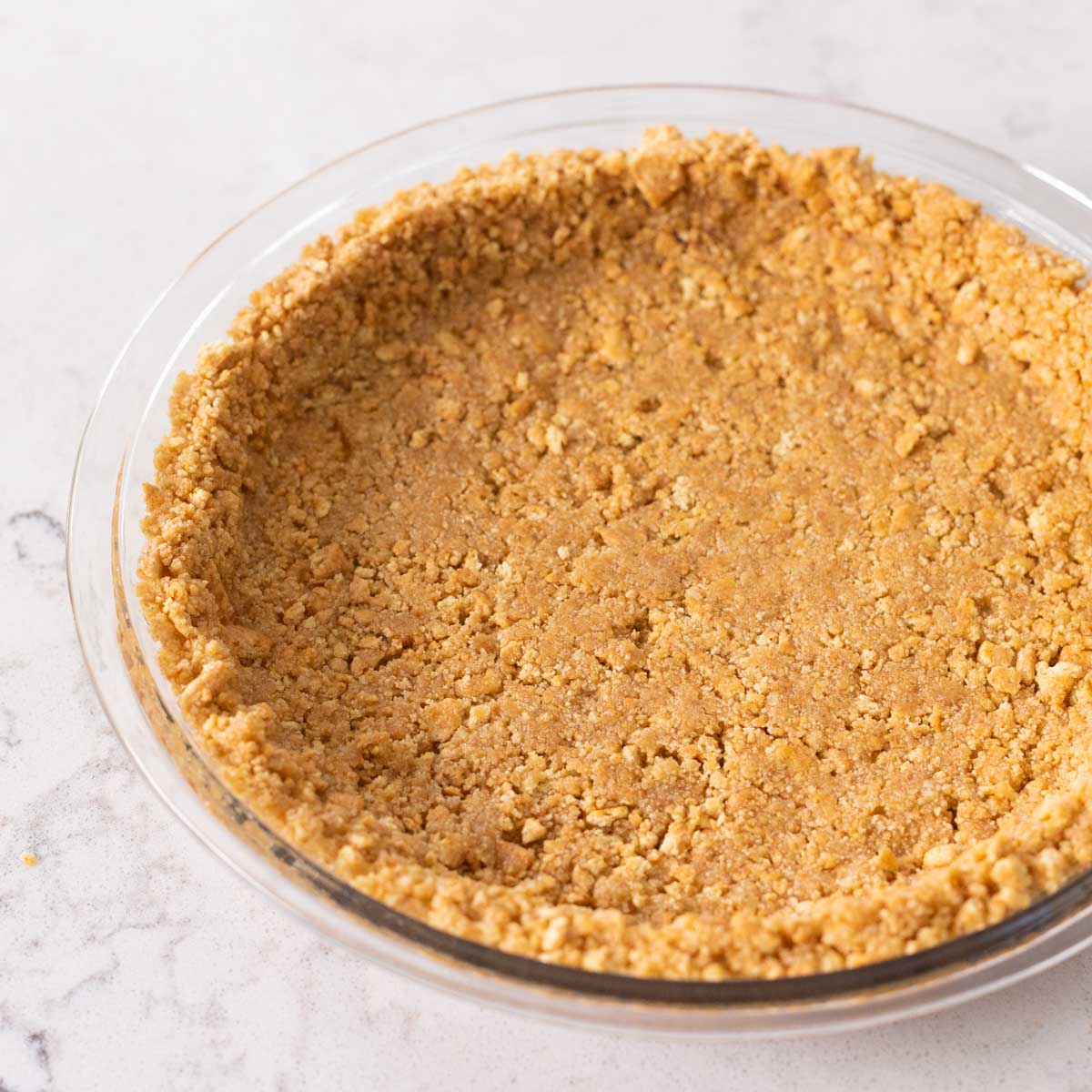 A graham cracker crust in a clear pie plate sits on the kitchen counter.