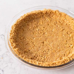 A clear pie plate has an empty graham cracker crust.