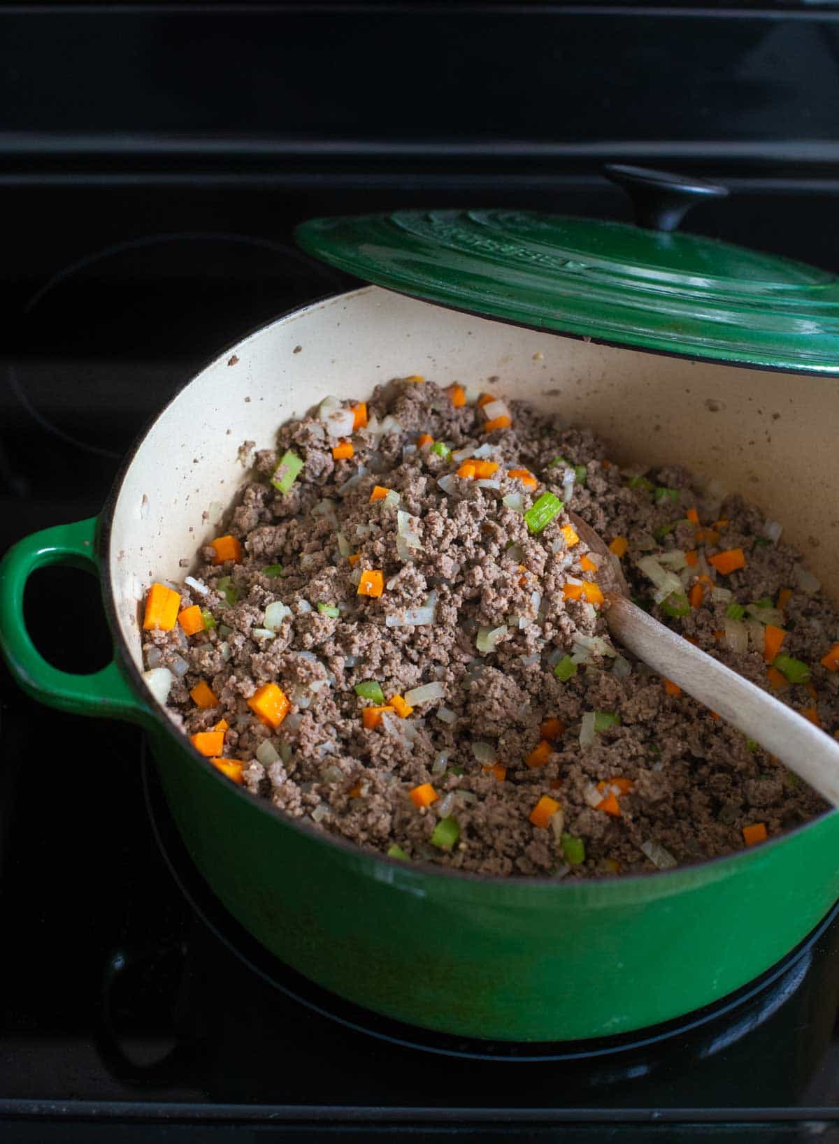 The ground beef is cooking in a green Dutch oven on the stovetop.