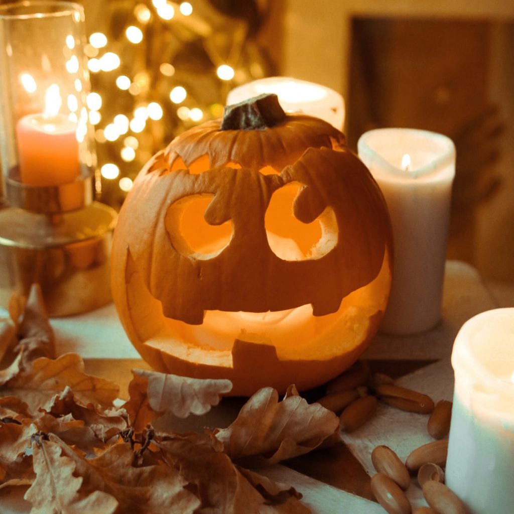 A Halloween jack-o-lantern has a silly smiles. Lit candles and fall leaves complete the scene.