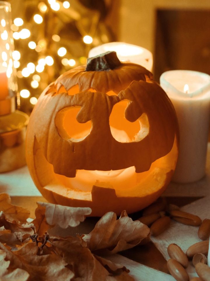A Halloween jack-o-lantern has a silly smiles. Lit candles and fall leaves complete the scene.