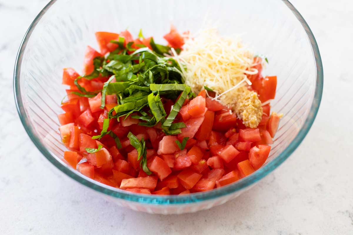 The fresh tomatoes and basil are in the mixing bowl with parmesan cheese.
