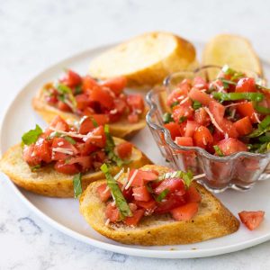 A plate of bruschetta pomodoro with a bowl of the tomato topping.