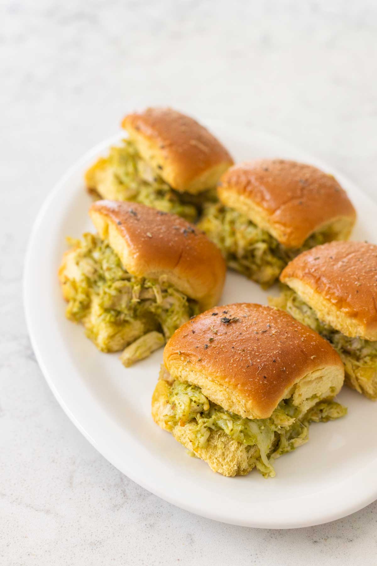 The baked pesto chicken sliders are on a white platter being served.
