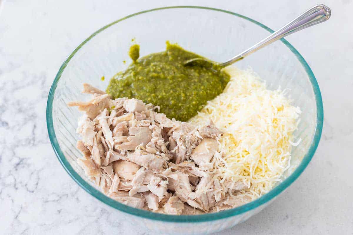 The shredded chicken, pesto, and cheese are in a bowl.