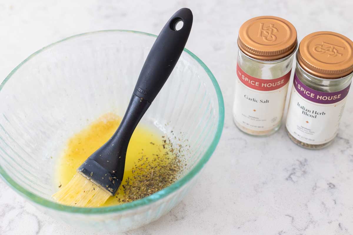 The bowl of melted butter has a pastry brush mixing in the seasonings.