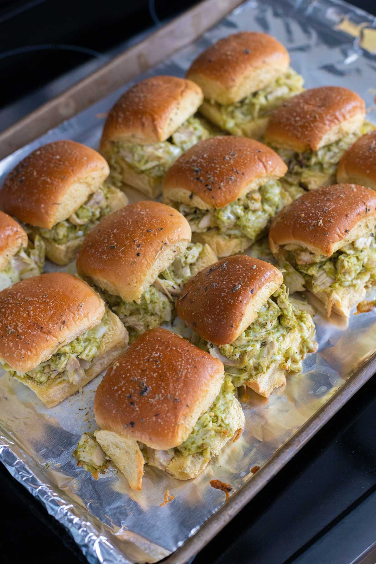 The baking pan of pesto chicken sliders just came out of the oven. The tops are golden brown and the cheese has melted.