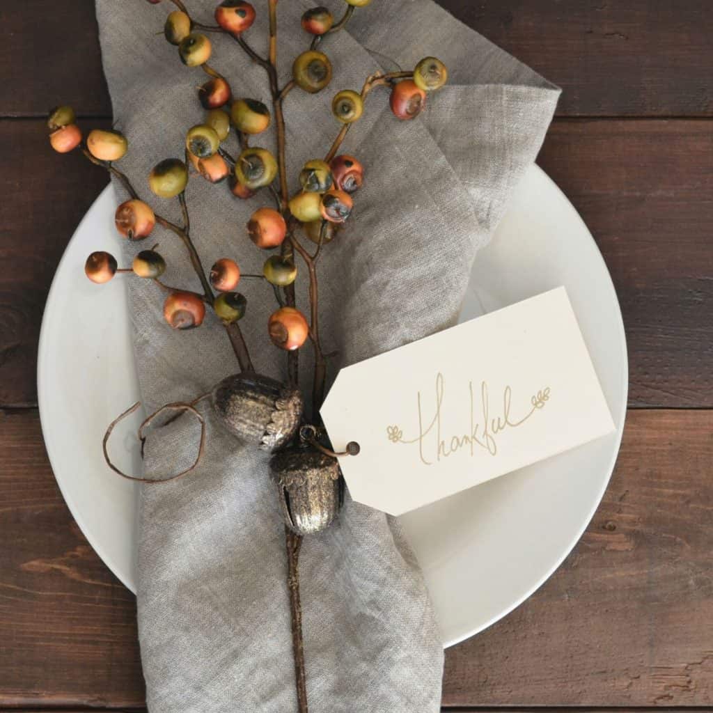 A white plate has a grey napkin and a sprig of orange berries with a tag that says "Thankful."