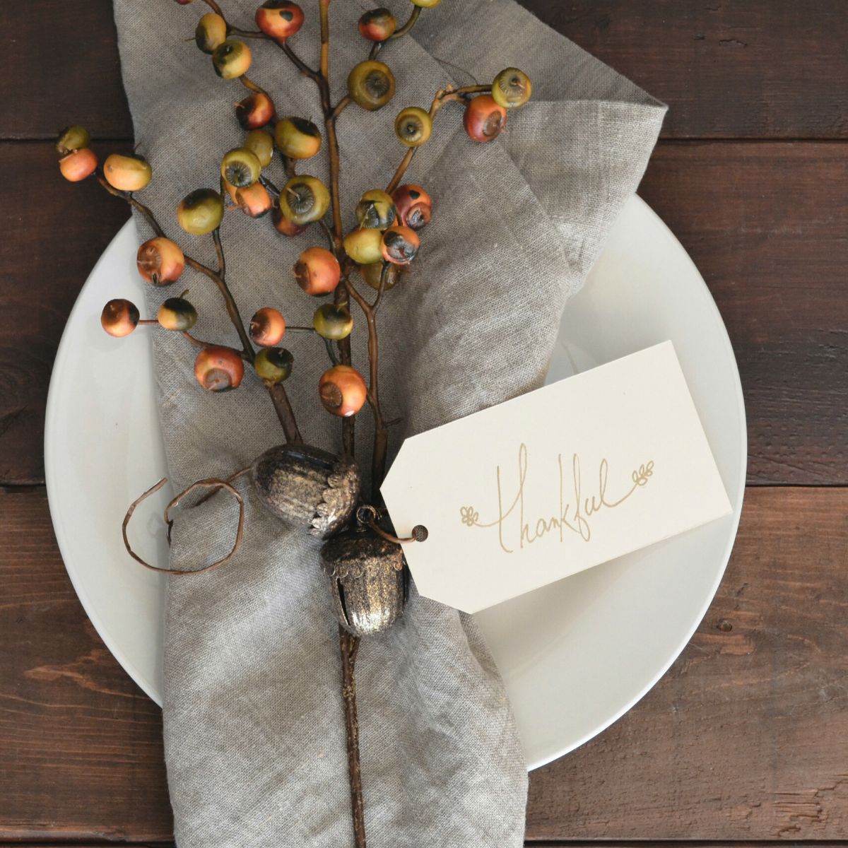 A white plate has a grey napkin and a sprig of orange berries with a tag that says "Thankful."