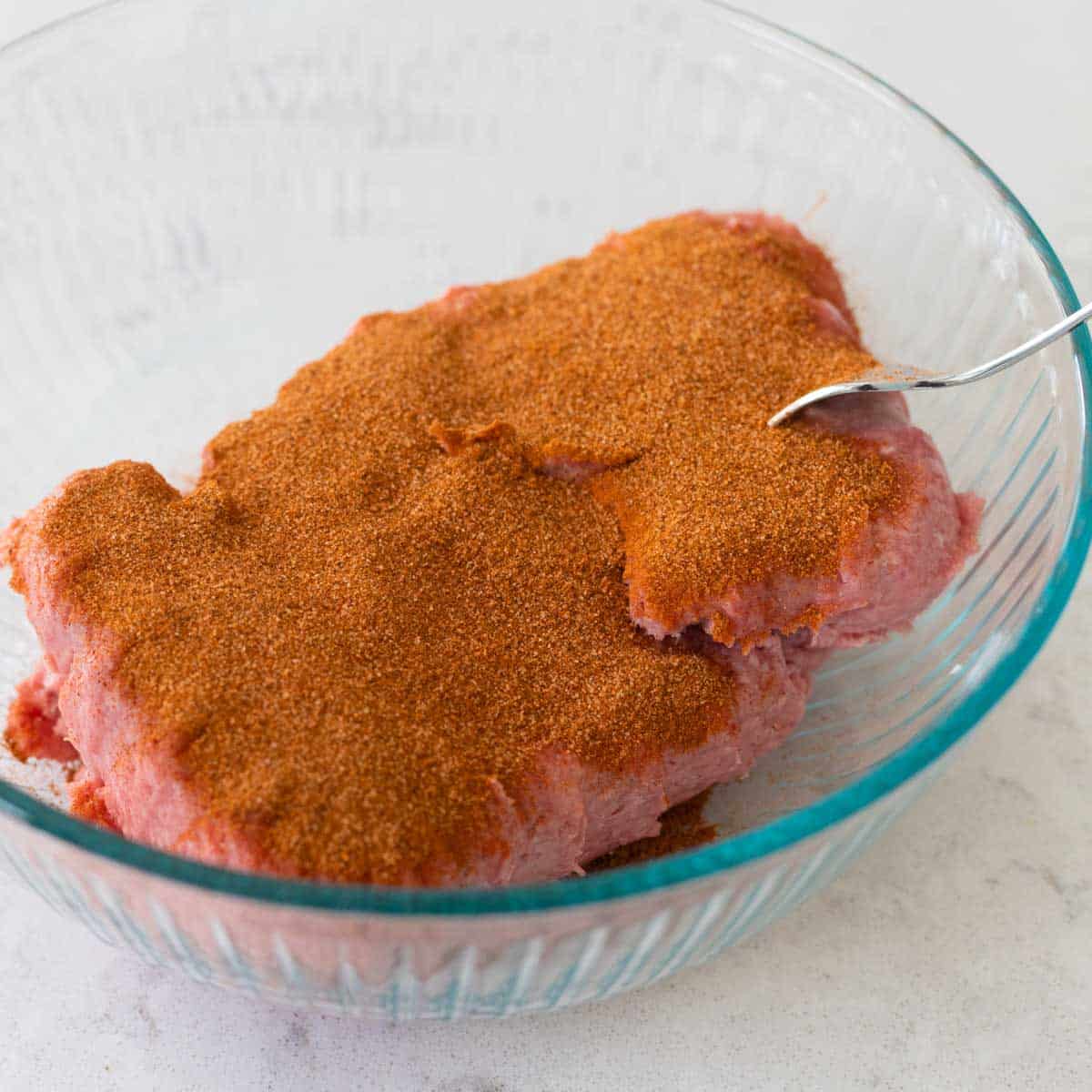 A mixing bowl has ground turkey covered in dry breakfast sausage seasonings.