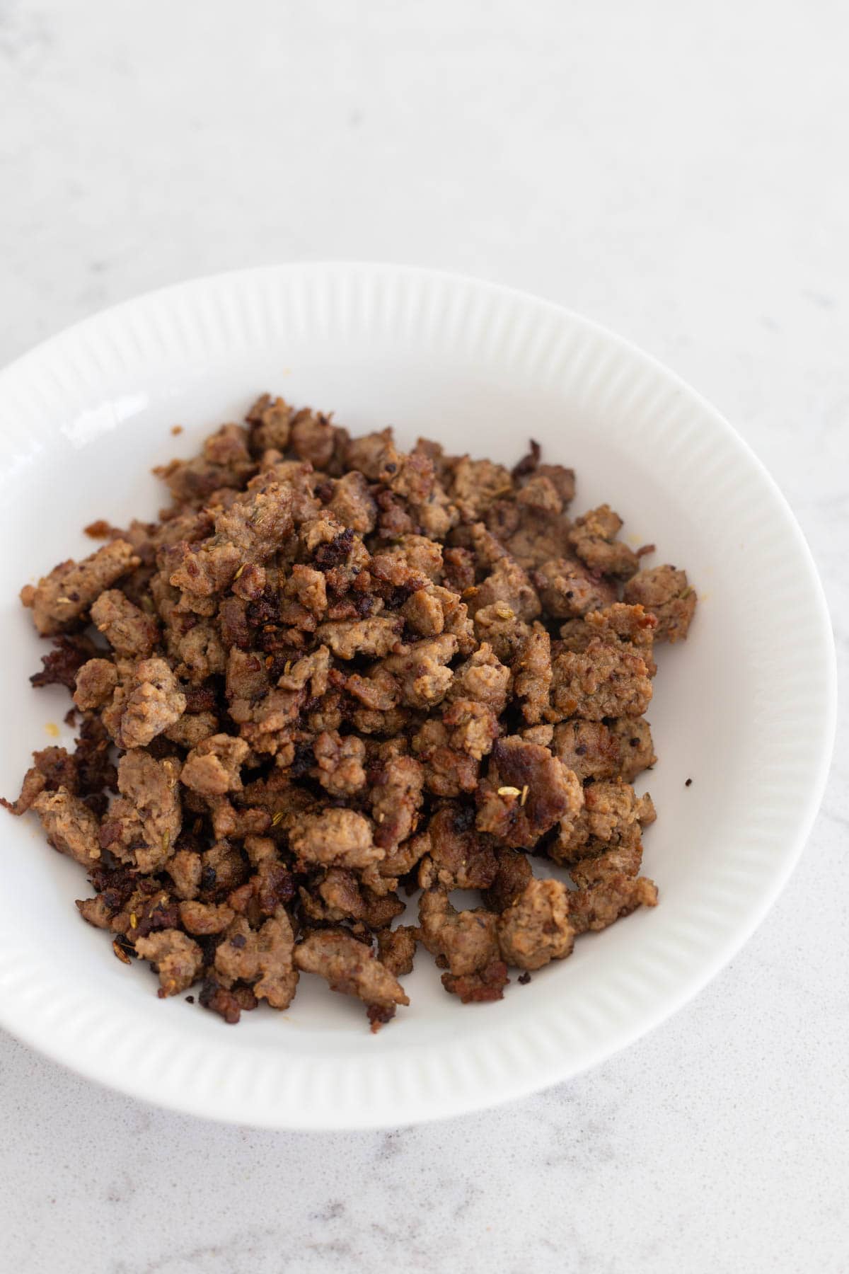 The turkey sausage was browned in a skillet and broken into crumbles. Now it is being served in a white bowl.