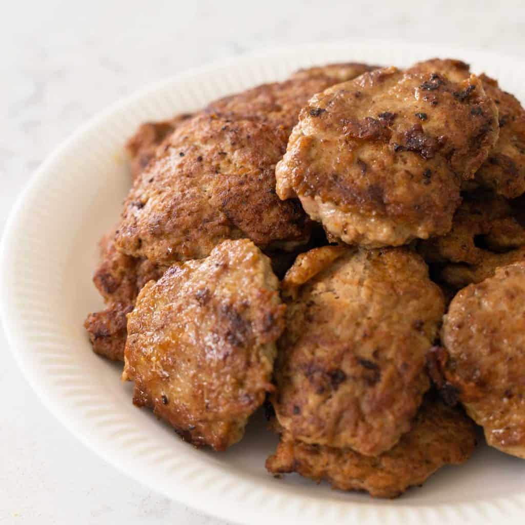 A white plate has turkey breakfast sausage patties piled high for serving.