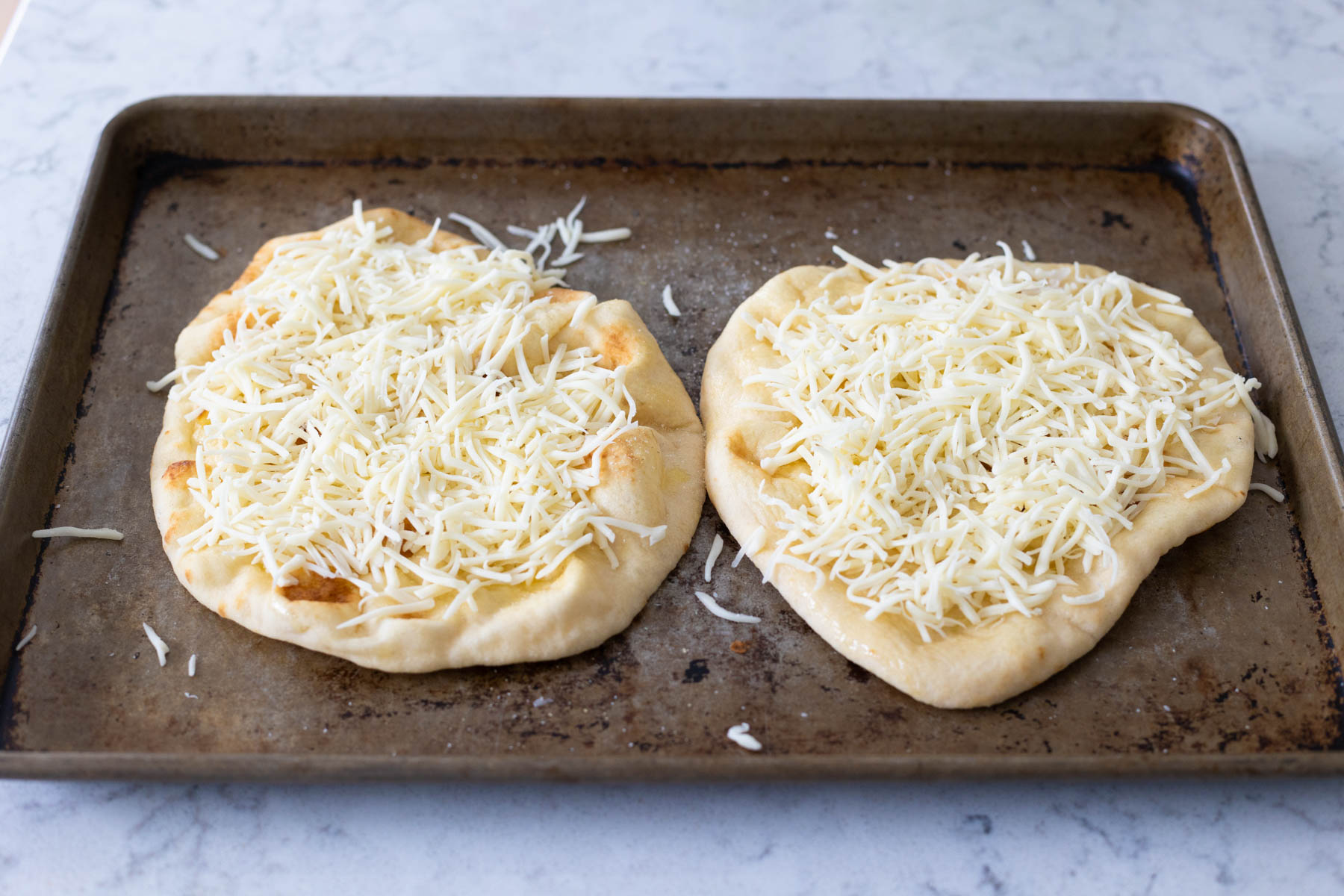 The shredded mozzarella has been sprinkled over the naan breads.