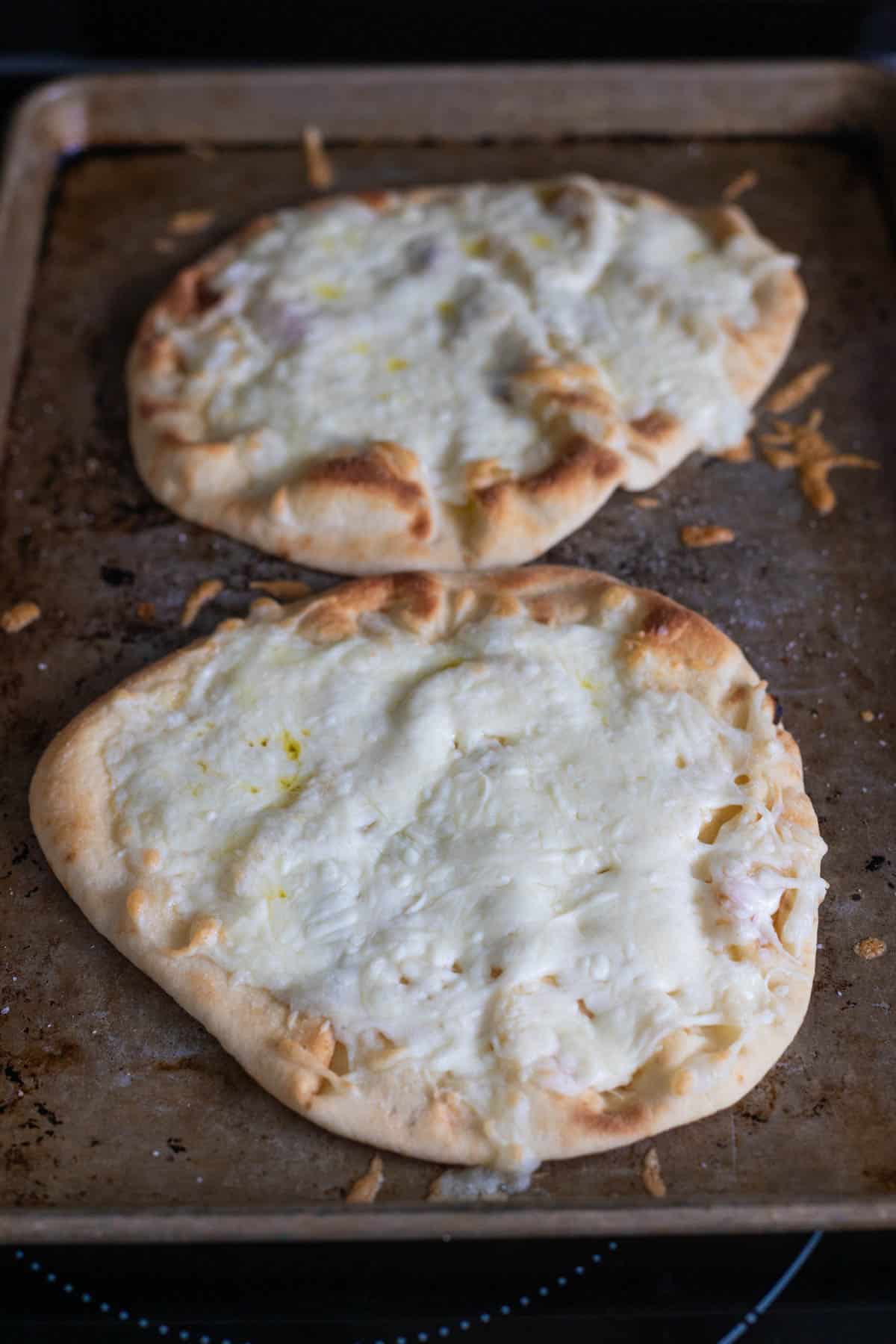 The naan breads have just come out of the oven, the shredded cheese has melted over the top and the edges are golden brown and bubbly.