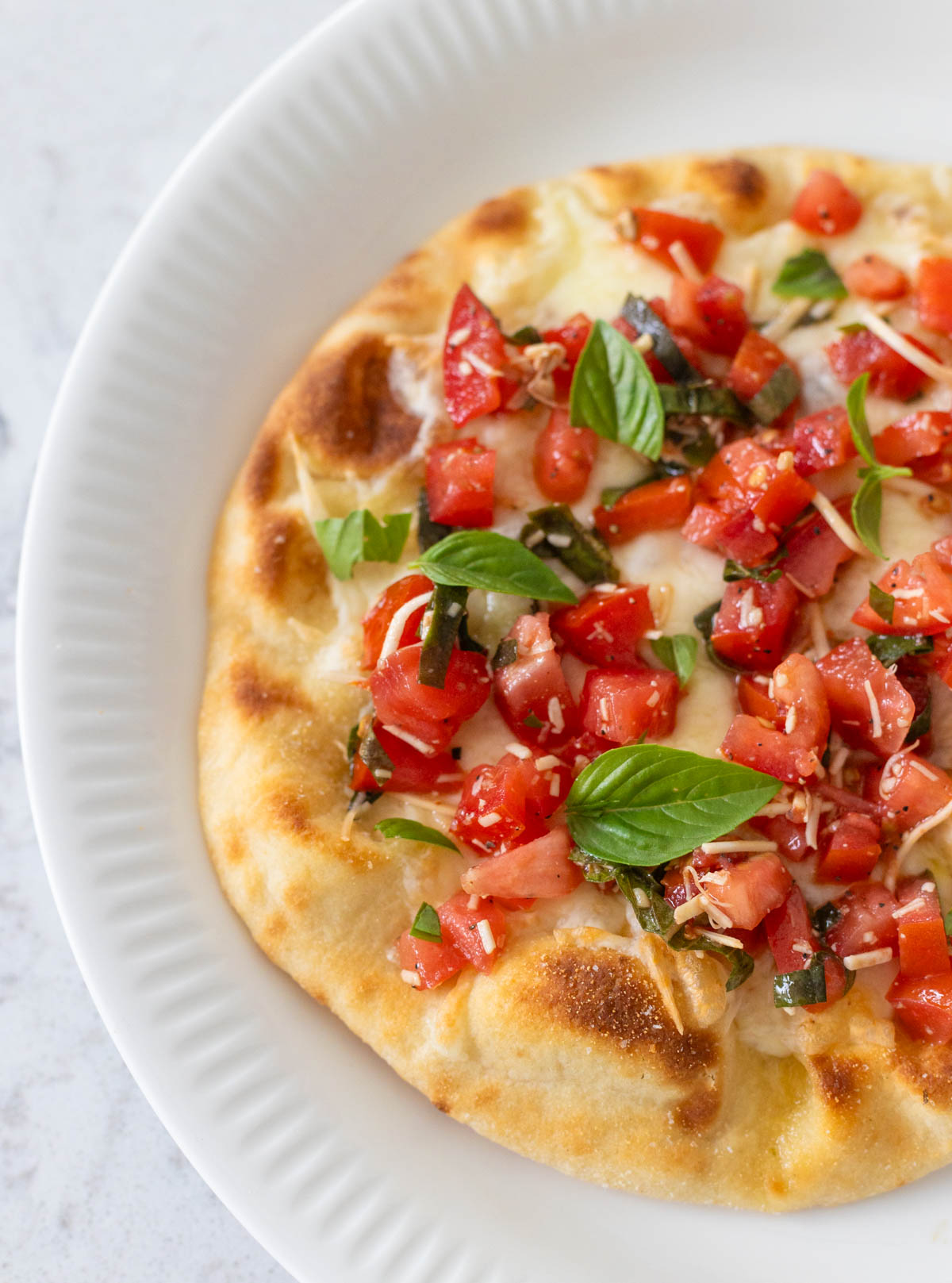 The bruschetta pizza is ready to be served with the fresh tomatoes and basil on top of the prepared naan bread.