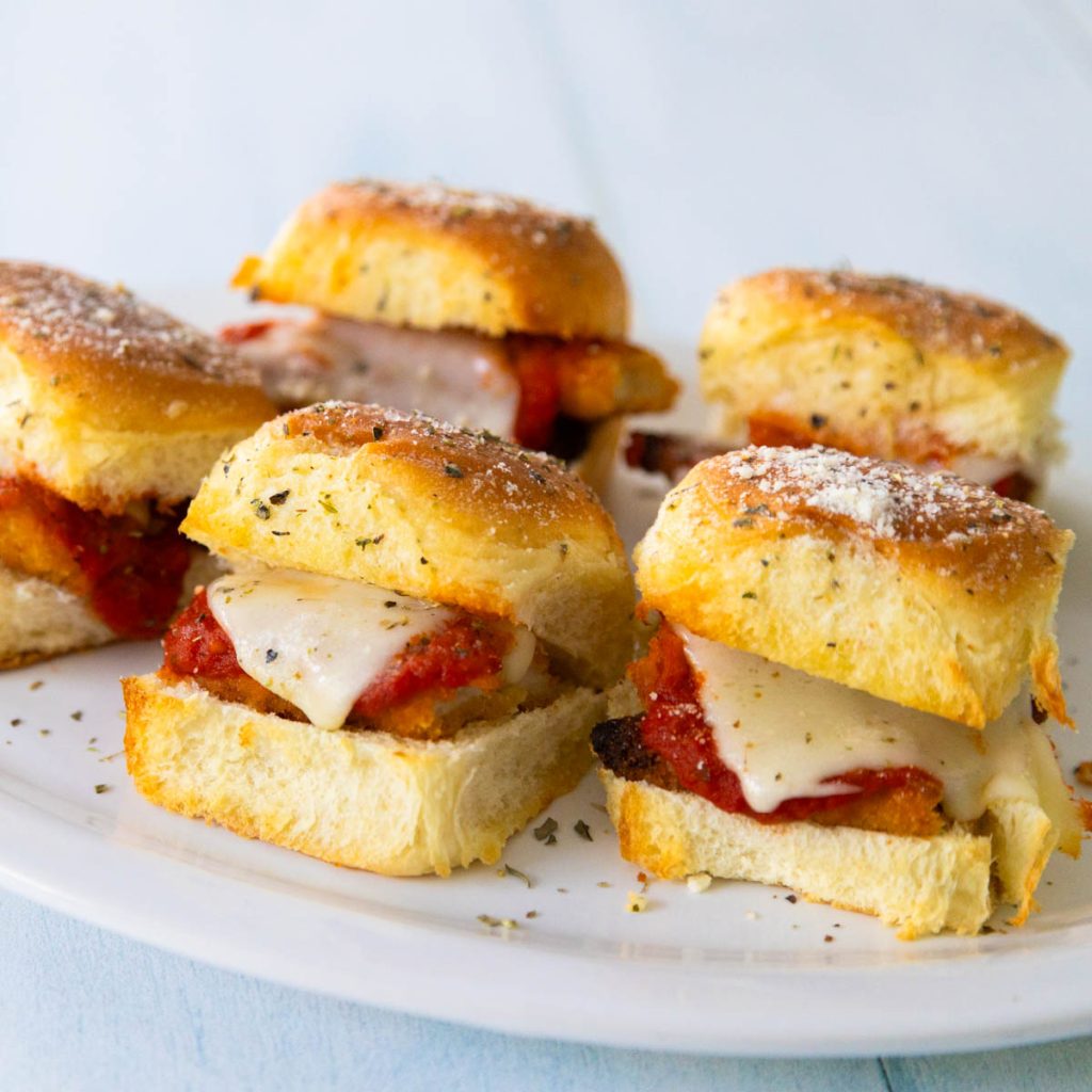 A white platter of chicken parm sliders shows the tomato sauce and melted cheese.