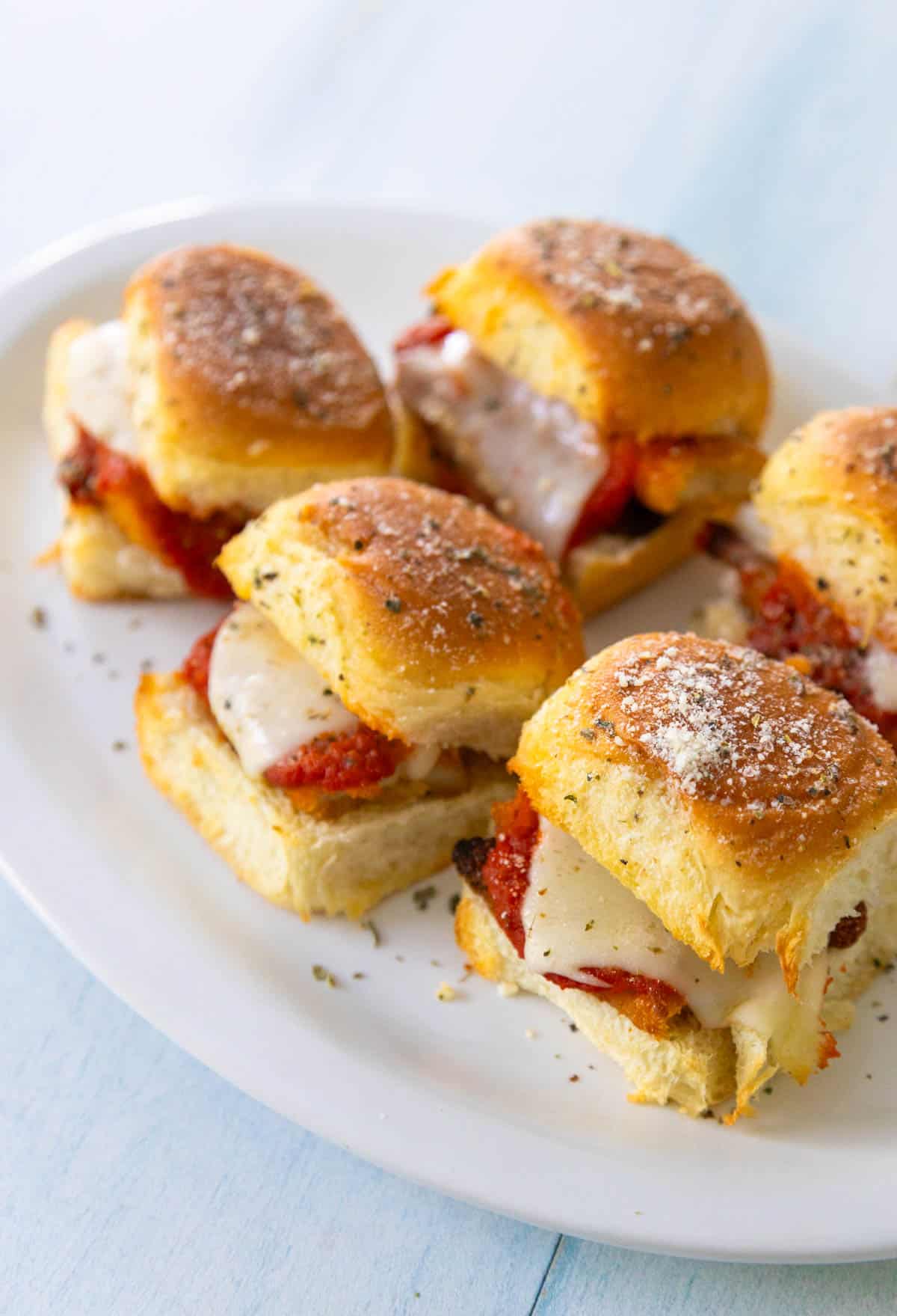 A white platter with several chicken parm sliders shows the tomato sauce and melted cheese for the filling.