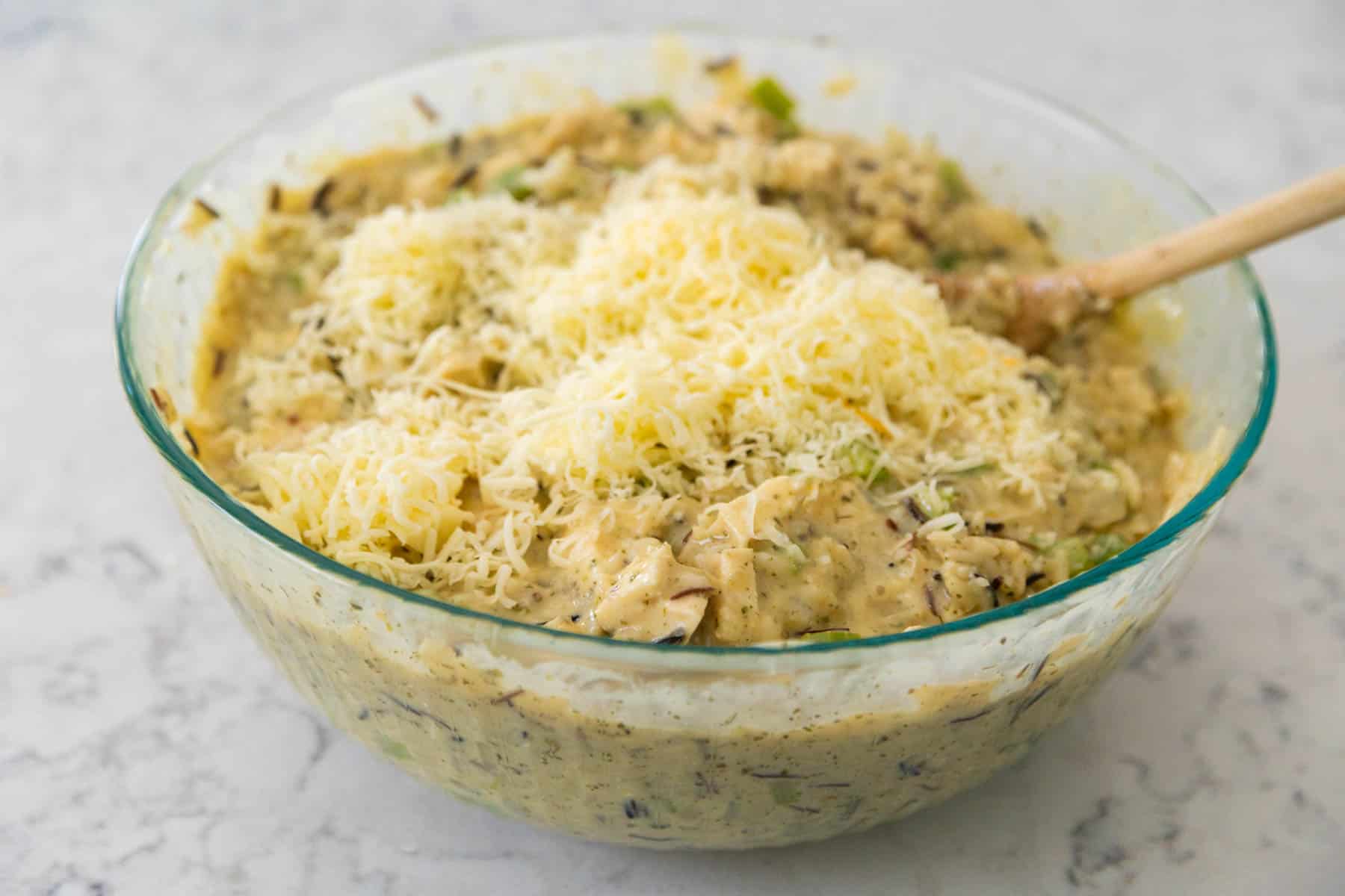 The shredded cheese is being stirred into the chicken filling in a mixing bowl.